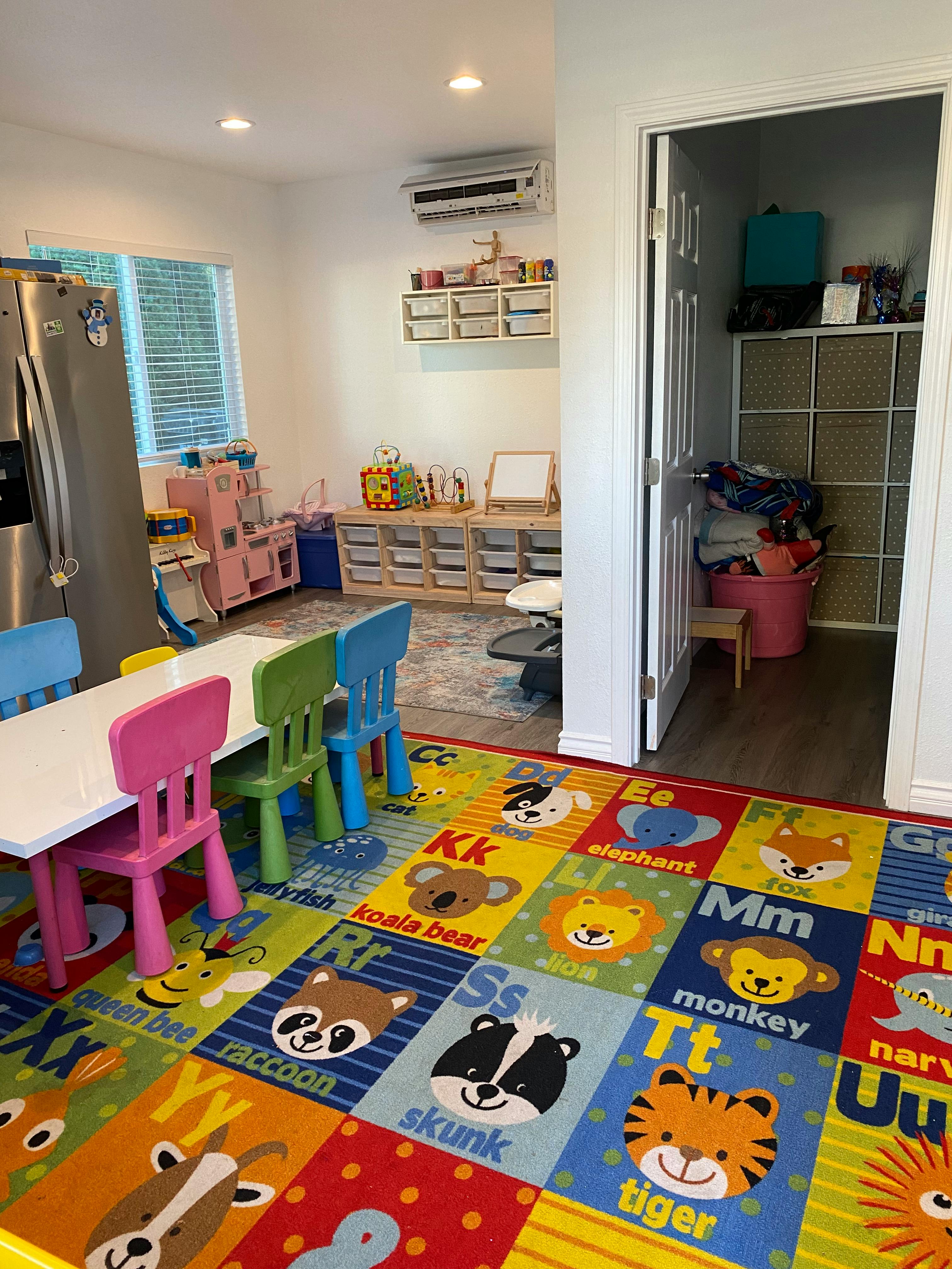 Children's play area with small table and chairs, alphabet rug, and storage