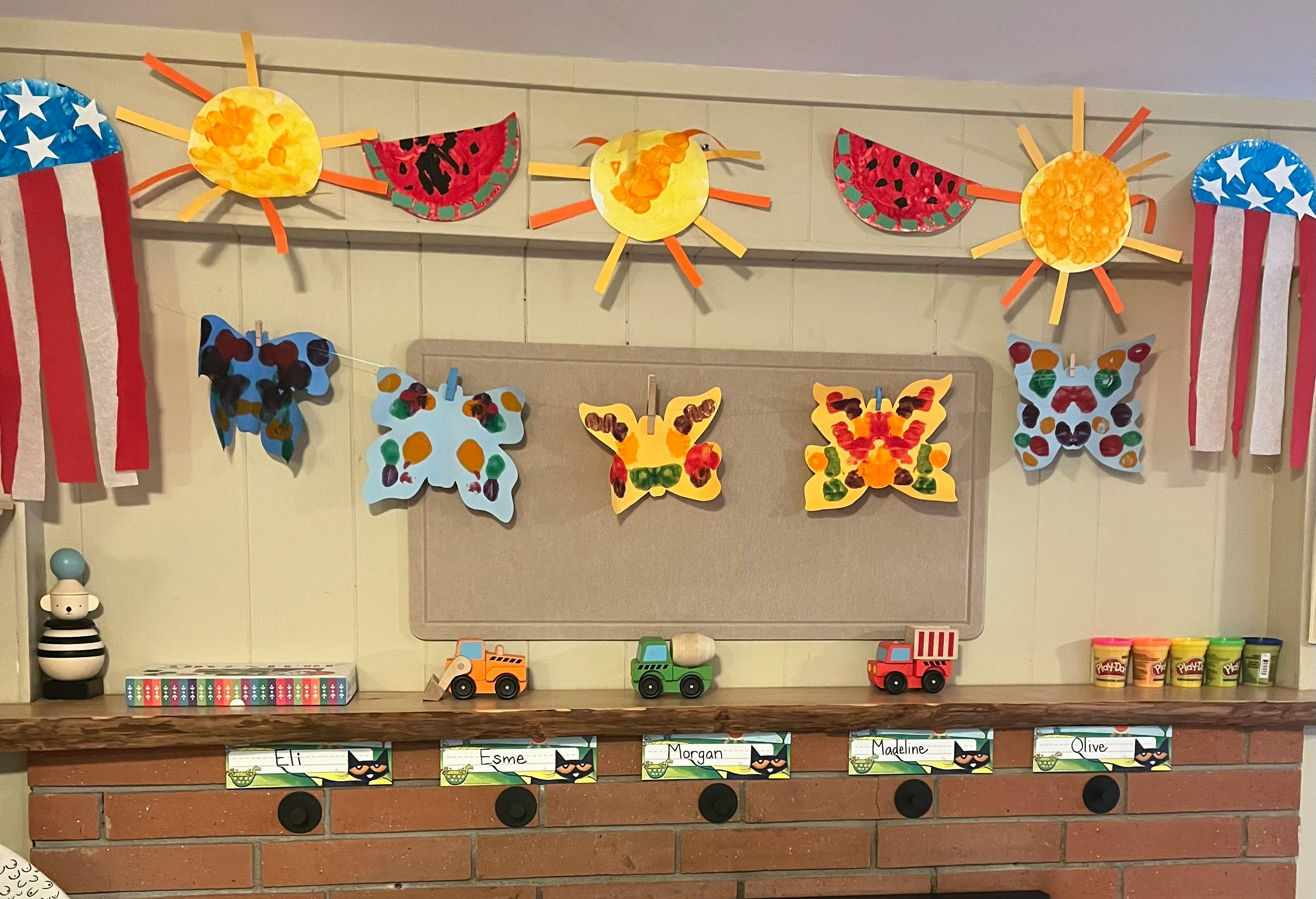 Children's artwork displayed on a wall, including suns, watermelons, and butterflies