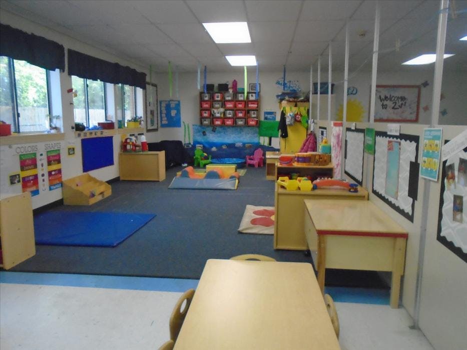 A colorful empty classroom with play equipment, tables, chairs, and bulletin boards