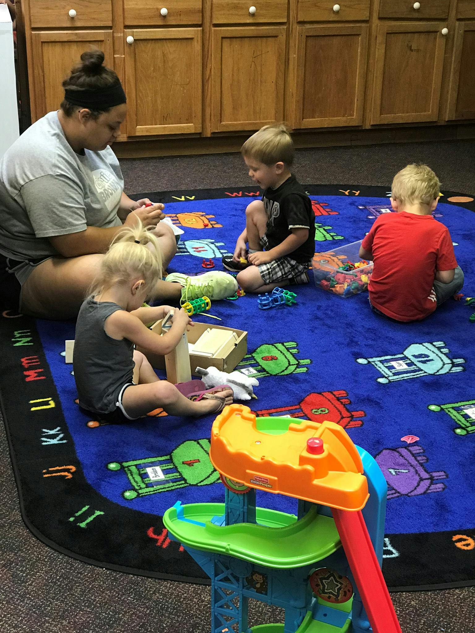 Adult and three children playing with toys on a rug