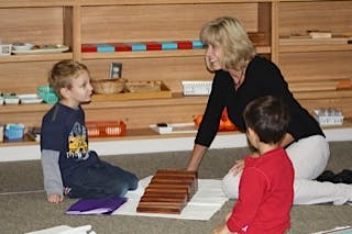 Adult and two children on floor with wooden blocks