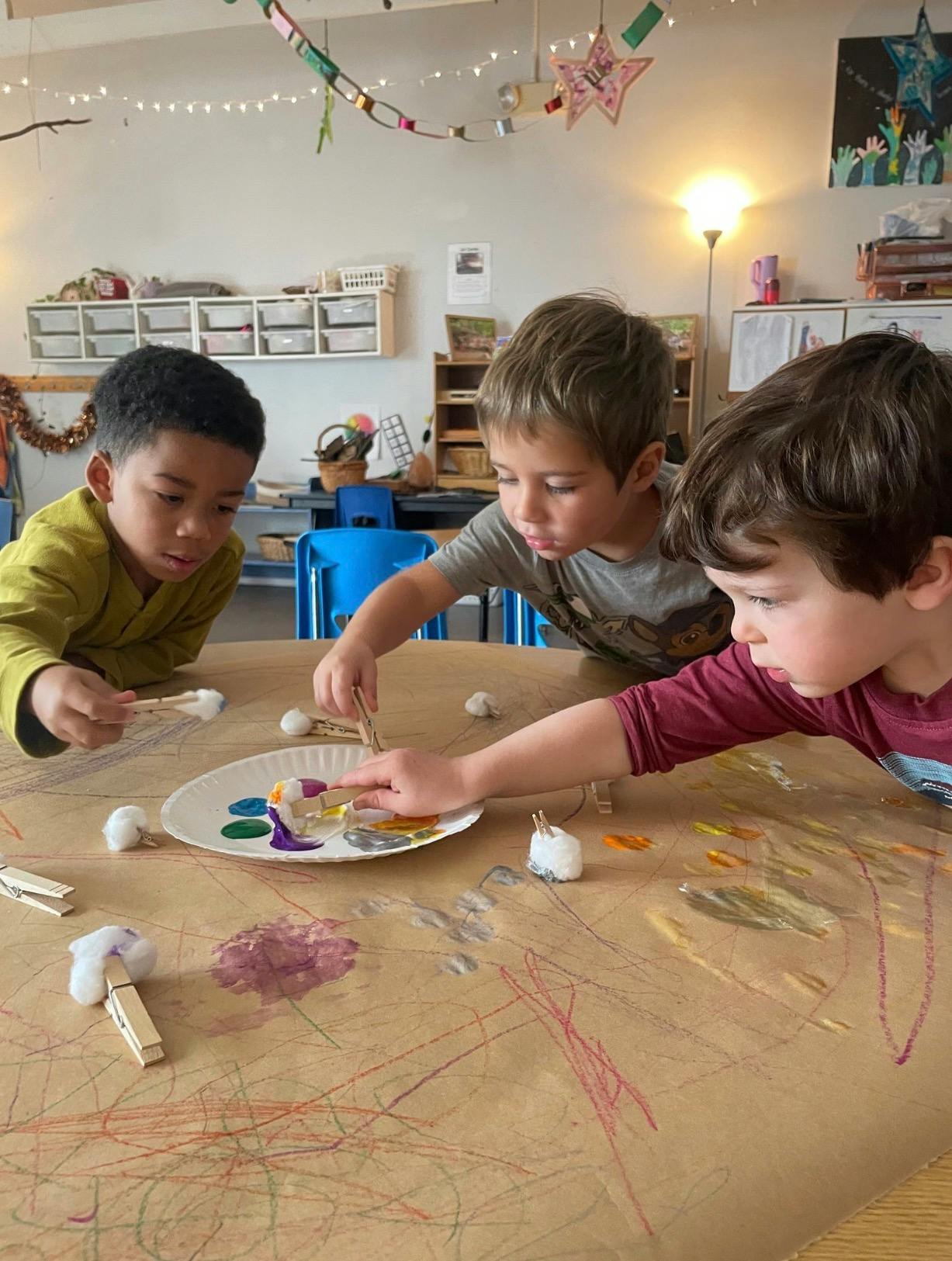 Three children painting with cotton balls and clothespins in a classroom