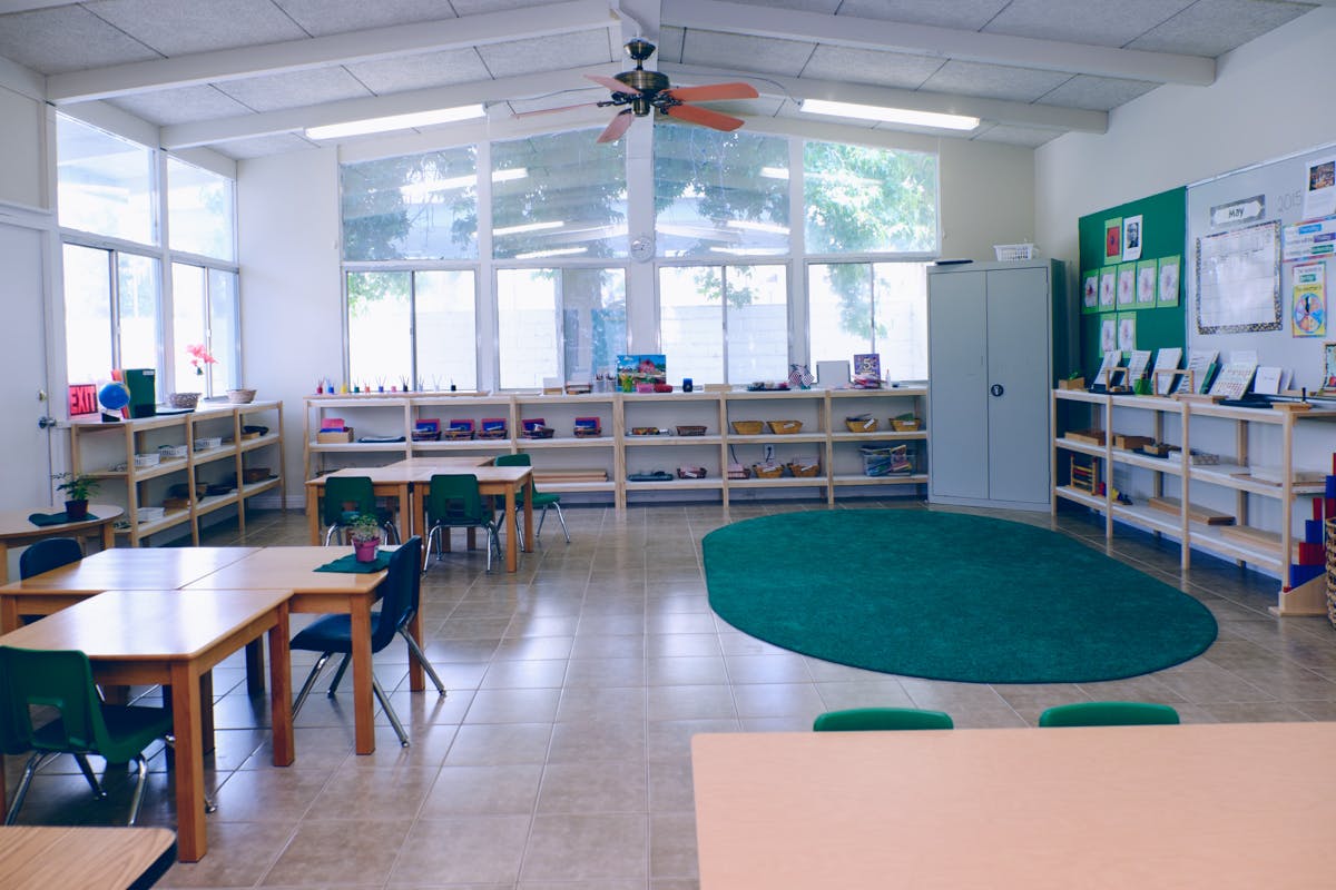Classroom with tables, chairs, shelves, and a green oval rug