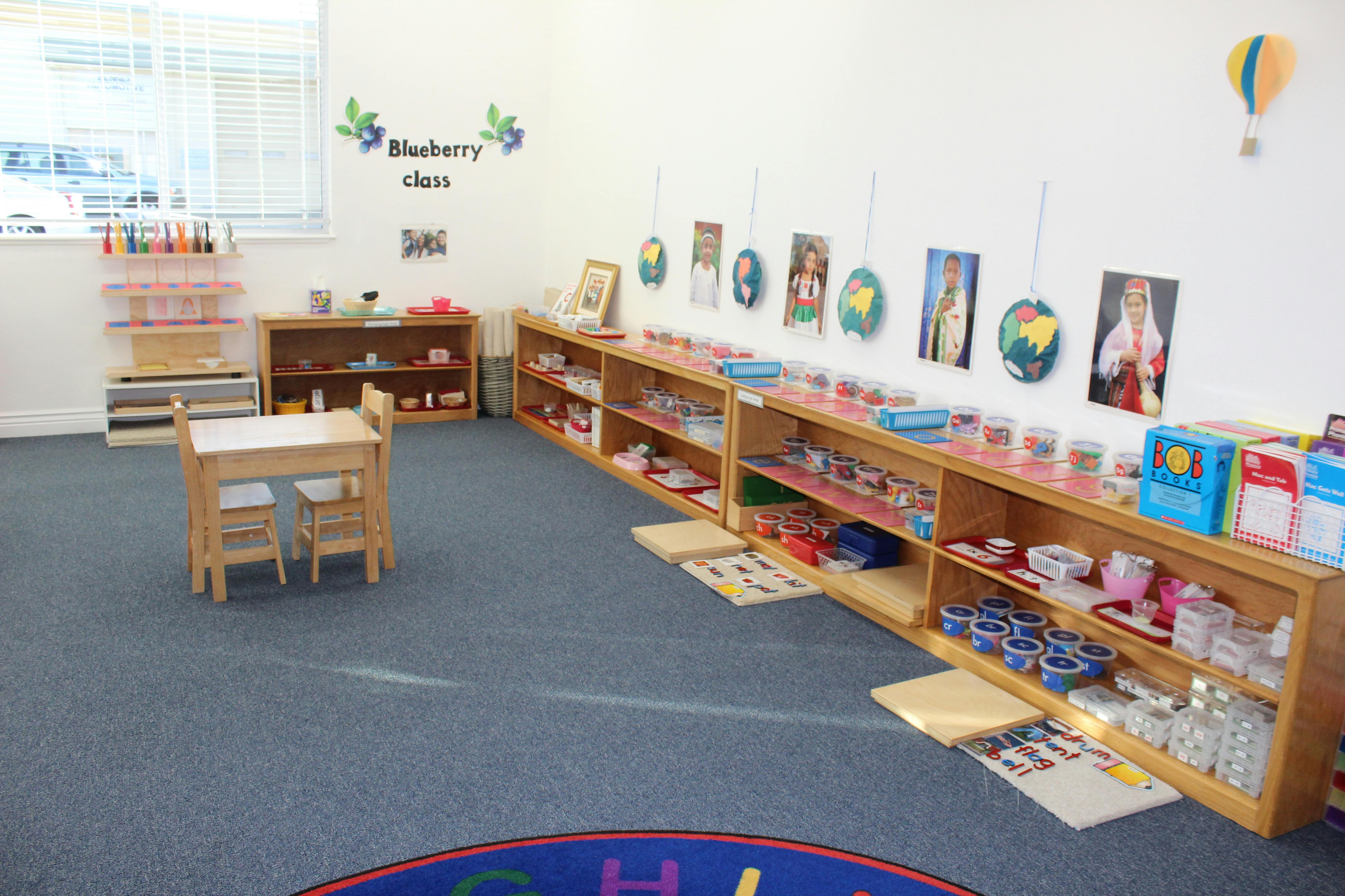 Classroom with shelves of learning materials and small tables, "Blueberry class" on wall