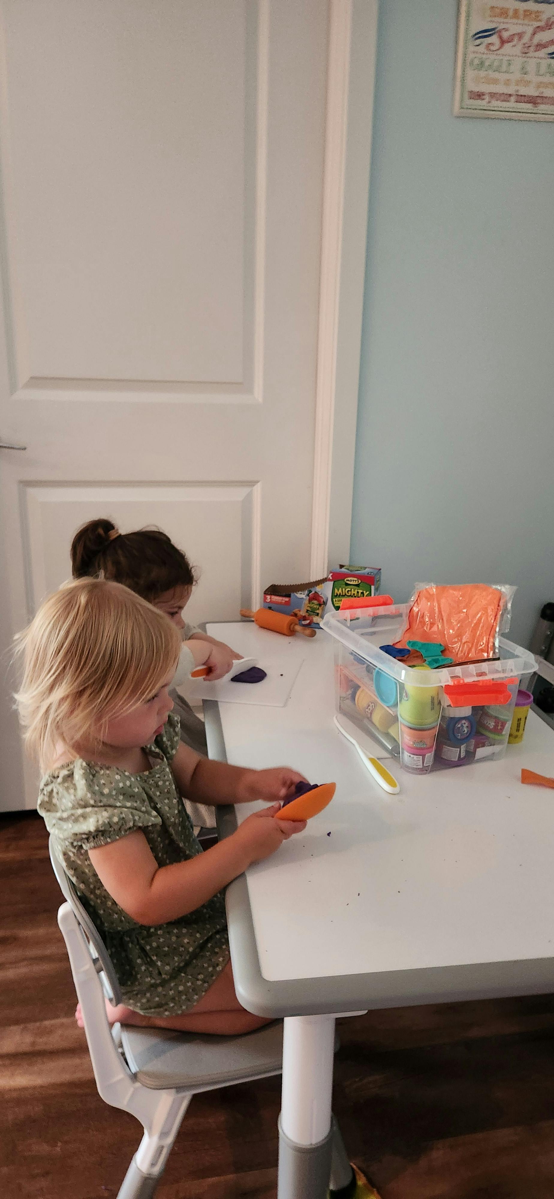 Two children sitting at a table playing with modeling clay