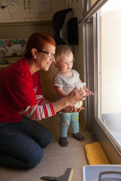 Person kneeling and child holding a spray bottle near a window