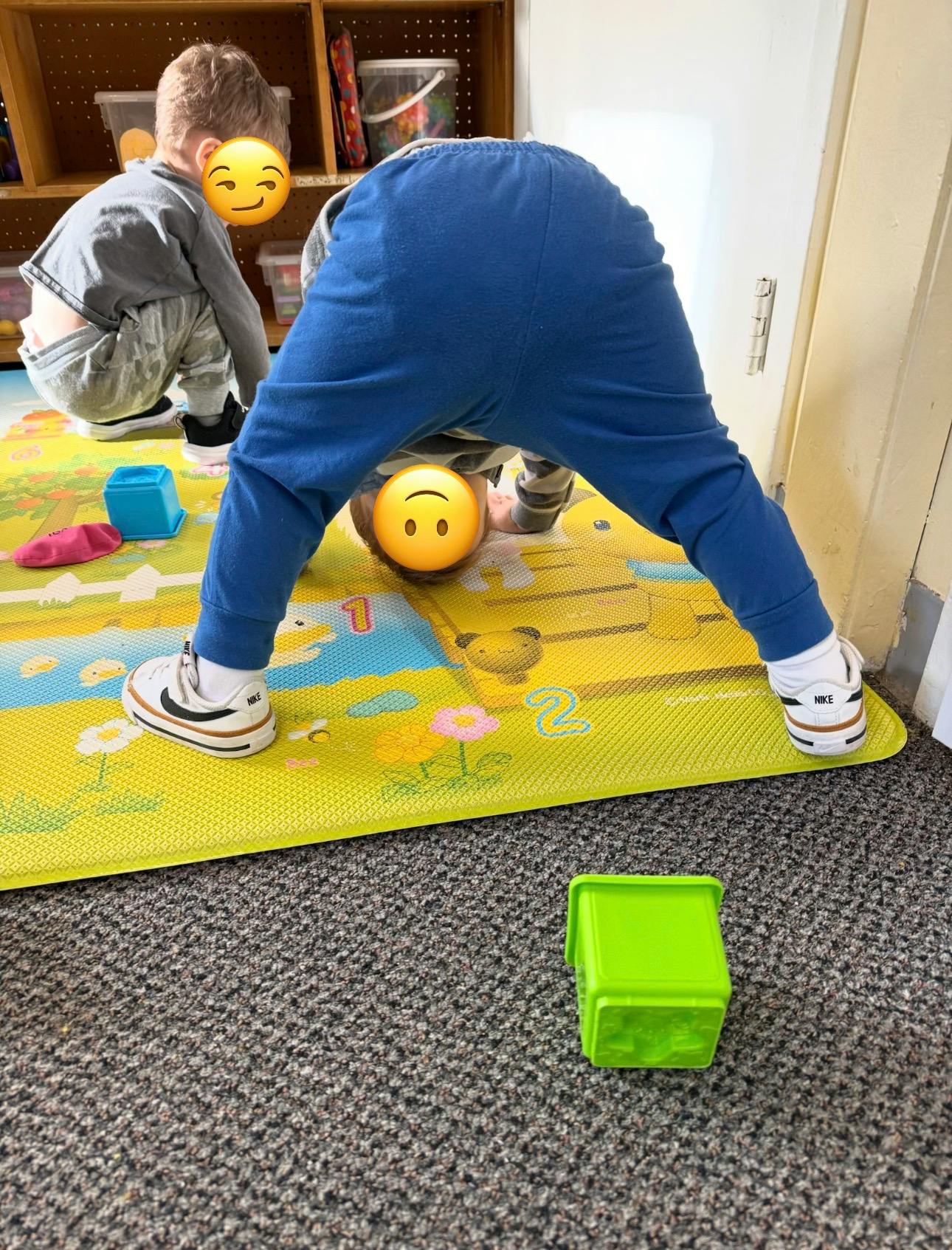 Child bending over with another child squatting nearby on a playmat