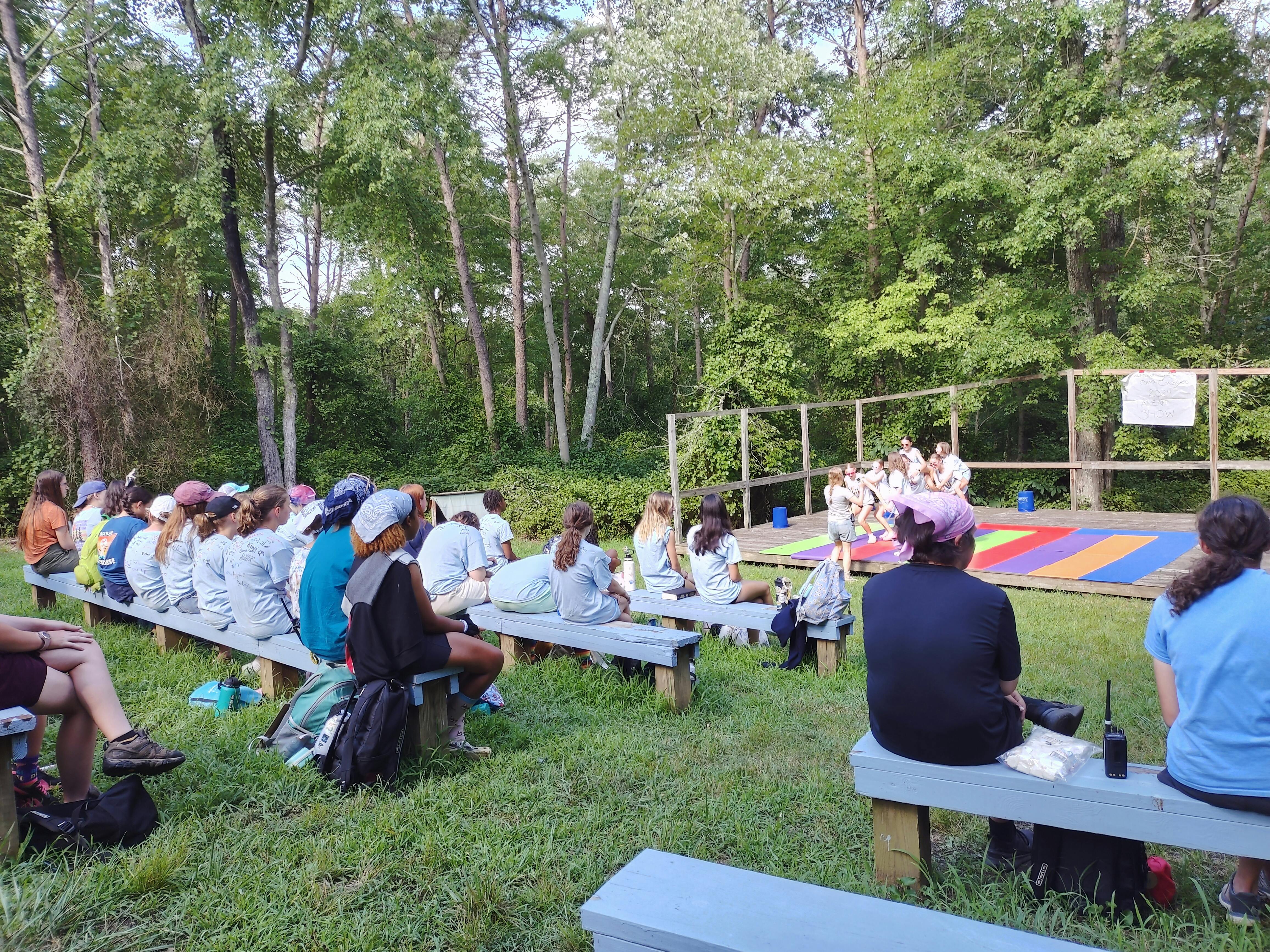 People sitting on benches watching a performance outdoors