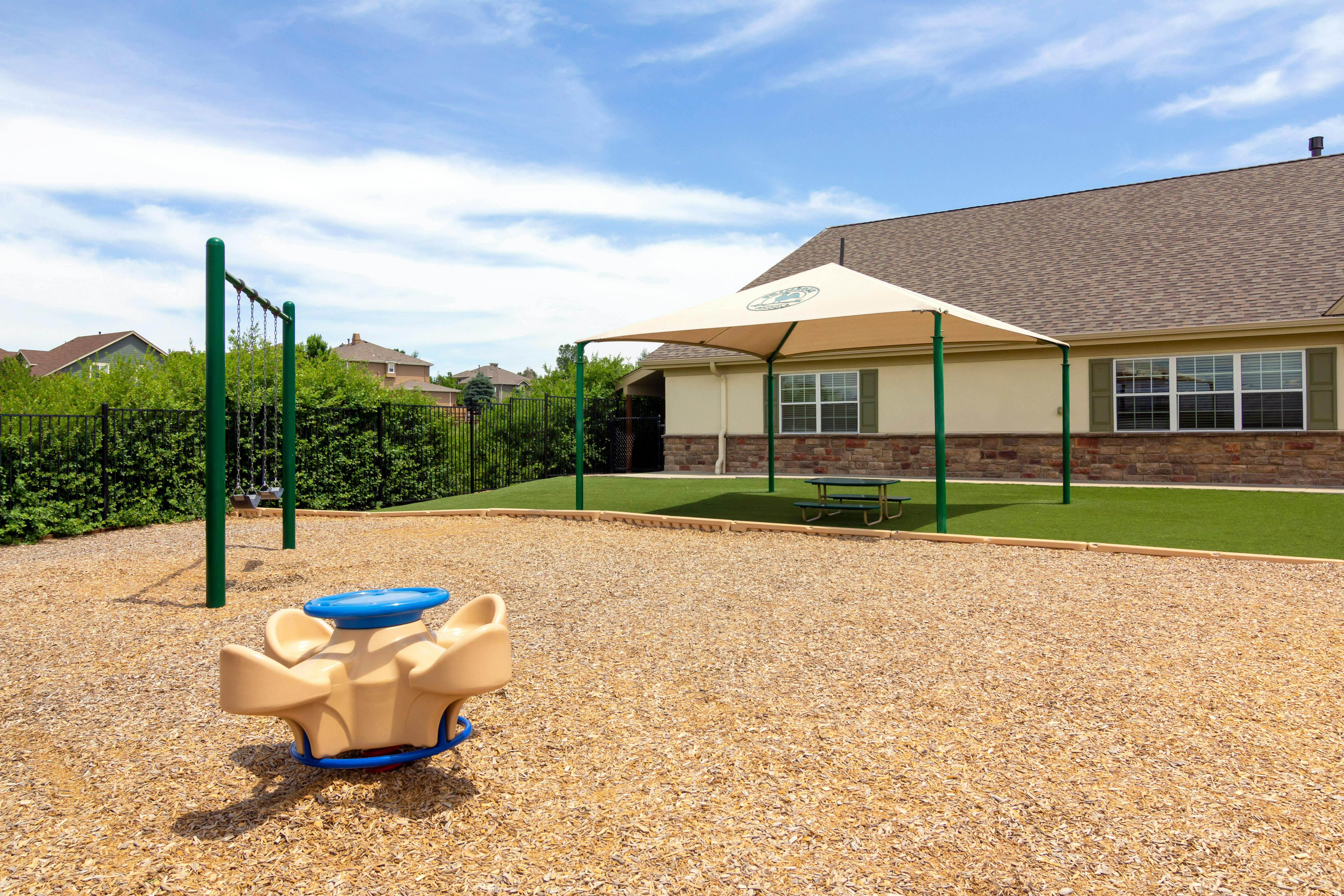 Swings, a merry-go-round, and picnic table under a canopy on a playground