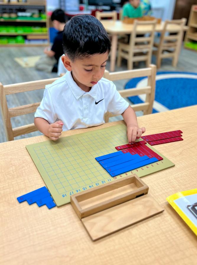 Child manipulating blue and red number rods on a grid board in a classroom