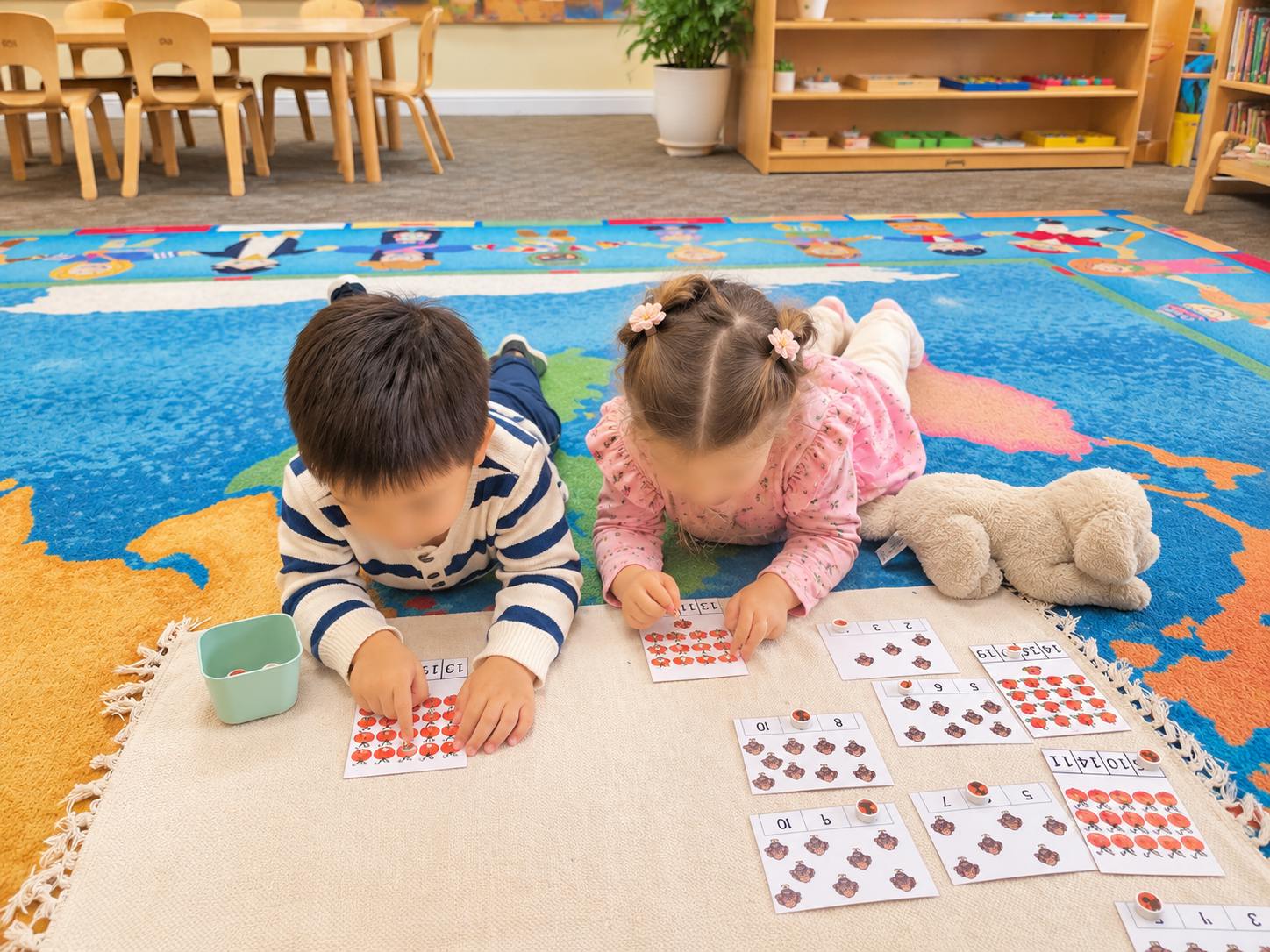 Two children lying on a classroom rug playing a matching number card game