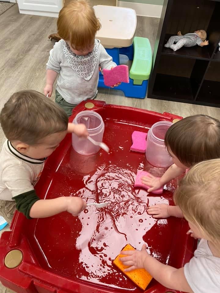 Children playing with sponges and water in a red bin