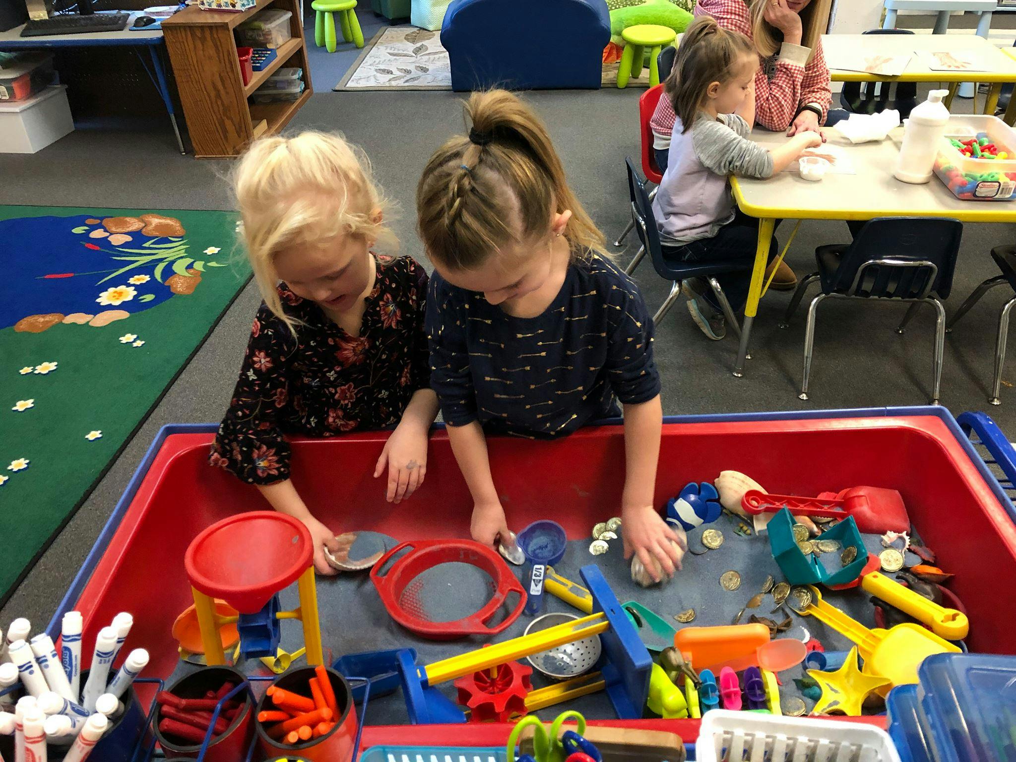 Two children playing in a sand table with toys