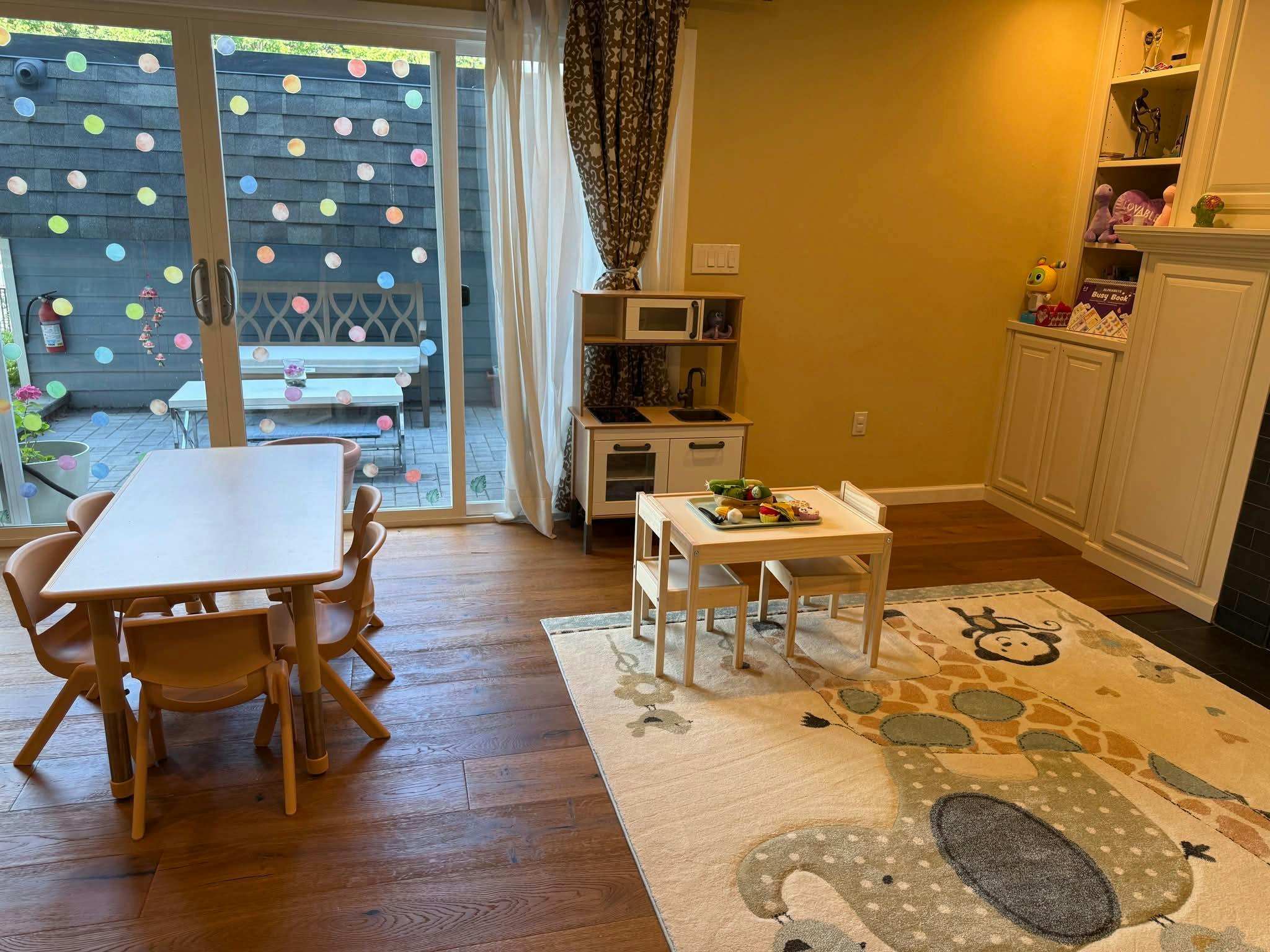 Playroom with child-sized tables and chairs, toy kitchen, and large rug
