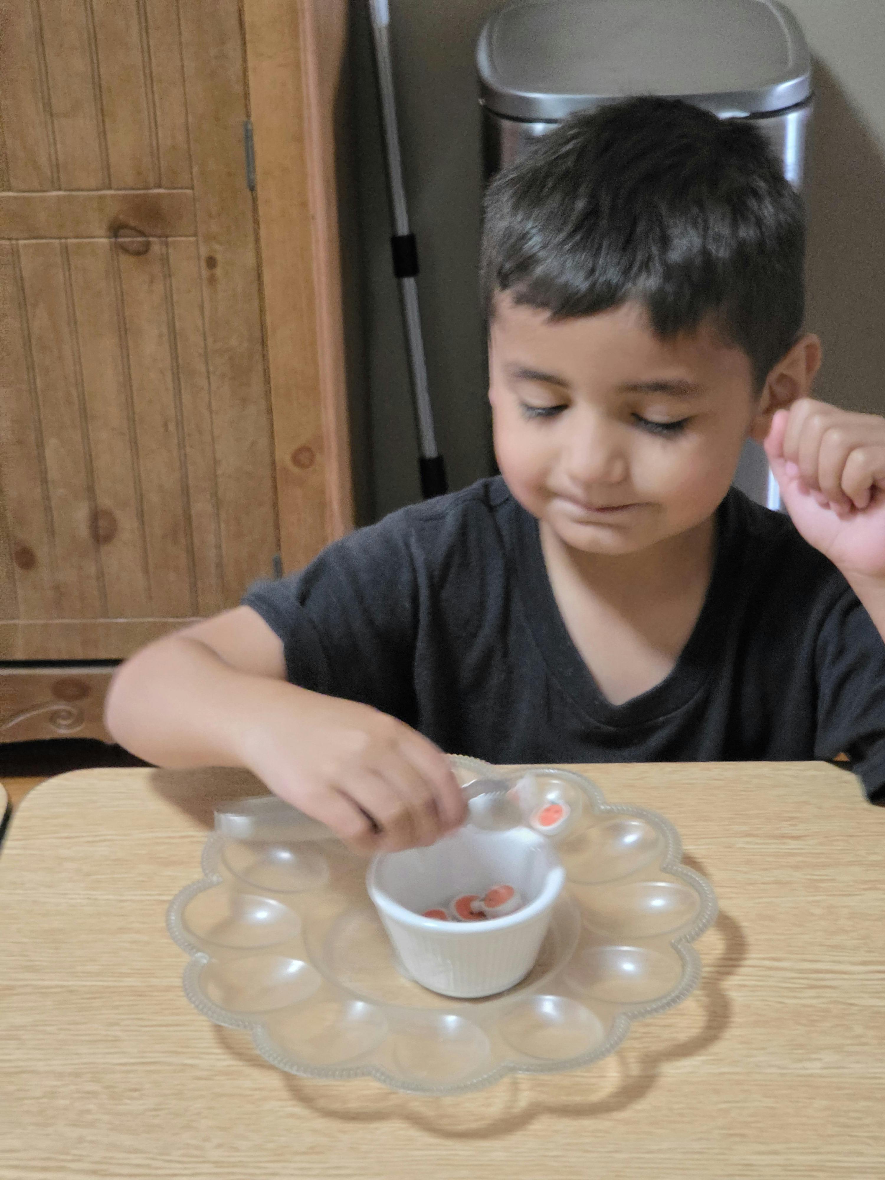 Child using tongs to place small tokens into a bowl