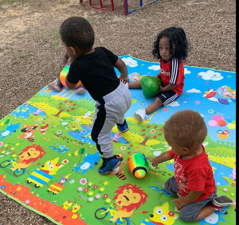 Three children playing with toys on a colorful mat outdoors
