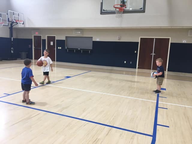 Three children playing with balls on a basketball court