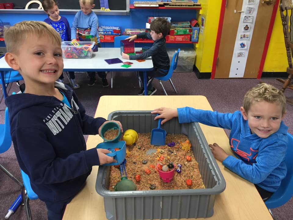 Two children playing with a sensory bin filled with sand and small toys