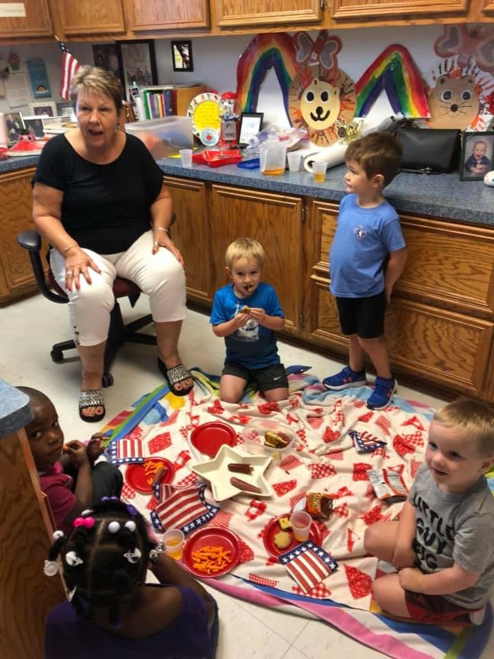 Adult and children gathered around a picnic blanket with food