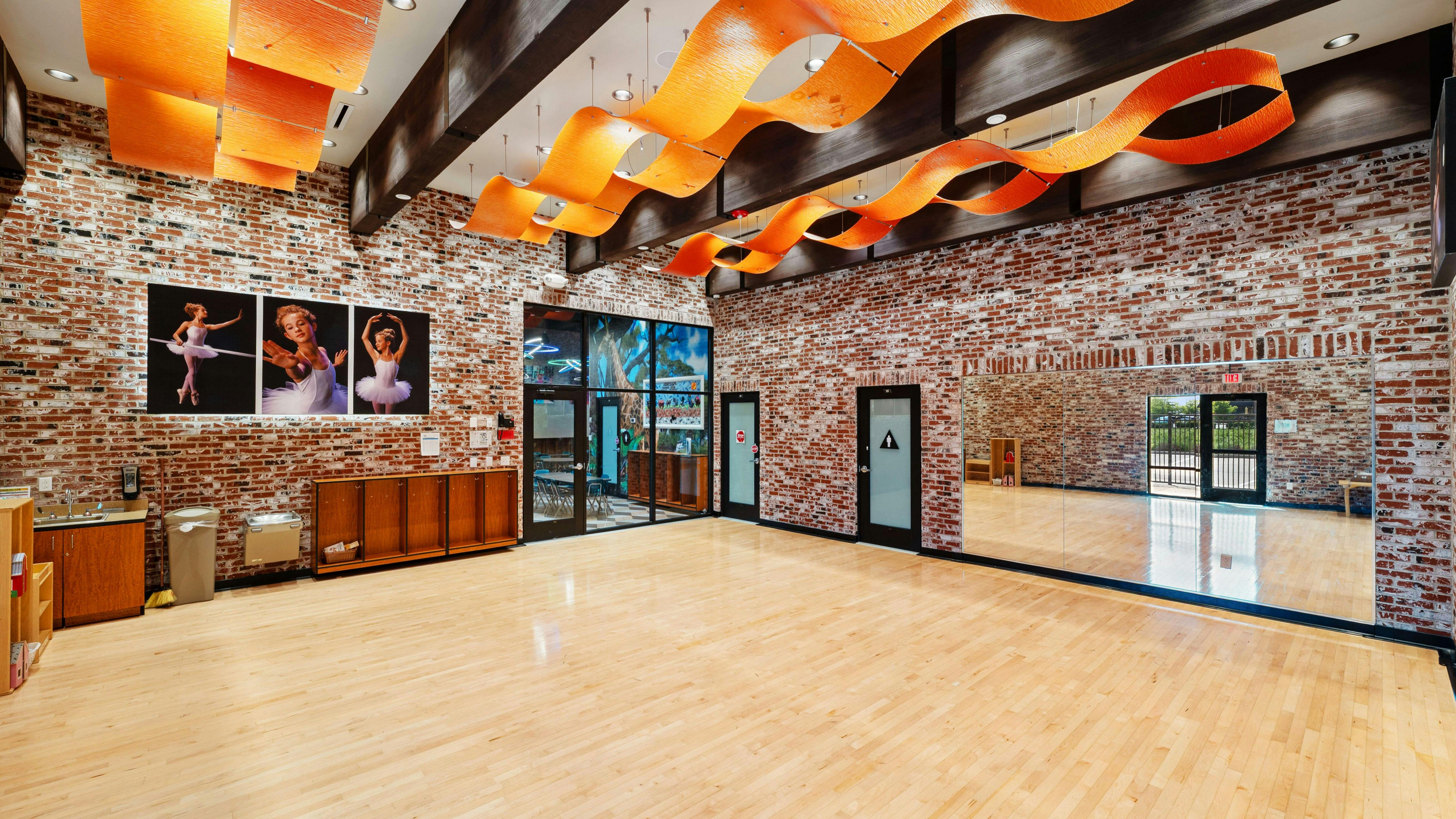 Empty studio with wooden floor, brick walls, a mirrored wall, and dance photos