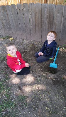 Two children kneeling on the ground outdoors