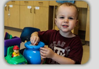 Child playing with a blue toy pot and other toys