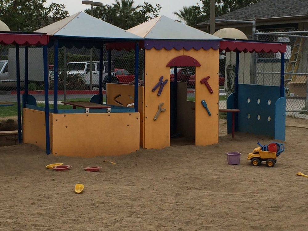 Play structure with sand, toys, and a small building with a canopy