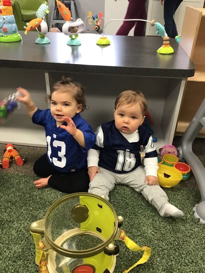 Two children sitting on a green carpet with toys