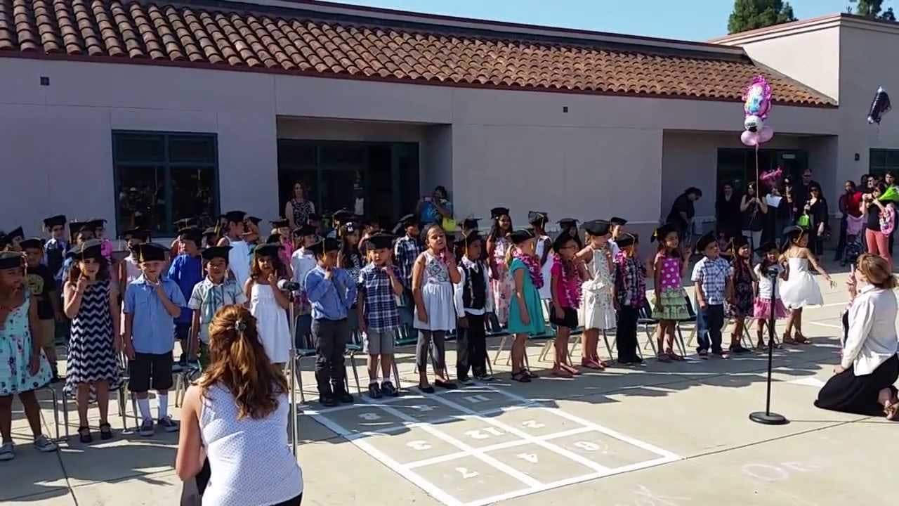 Children standing in a line outdoors with an adult kneeling in front