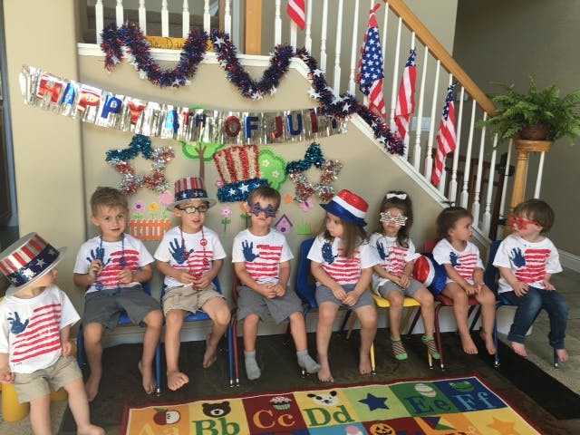 Children in patriotic shirts and hats sitting in front of a decorated wall