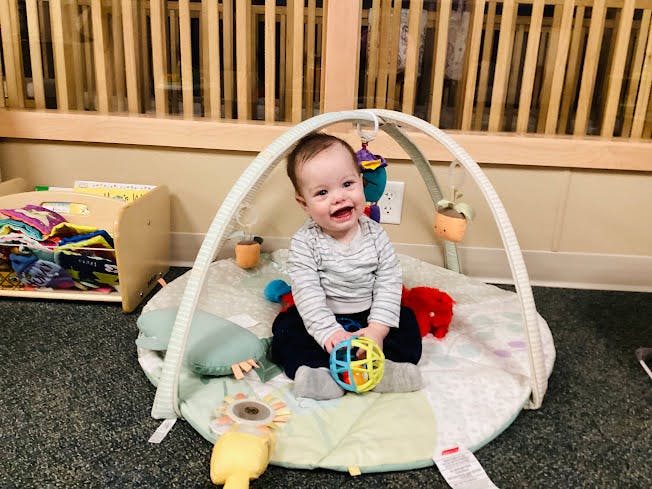 Child sitting on a play mat with a toy, looking at the camera