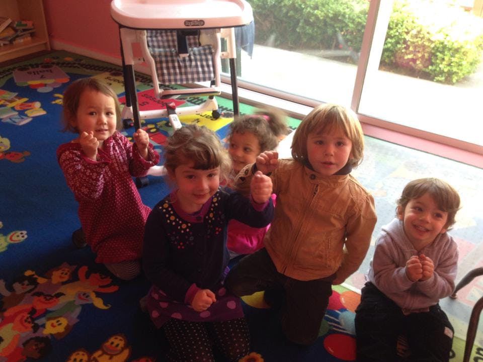 Five children sitting on a colorful rug in a classroom