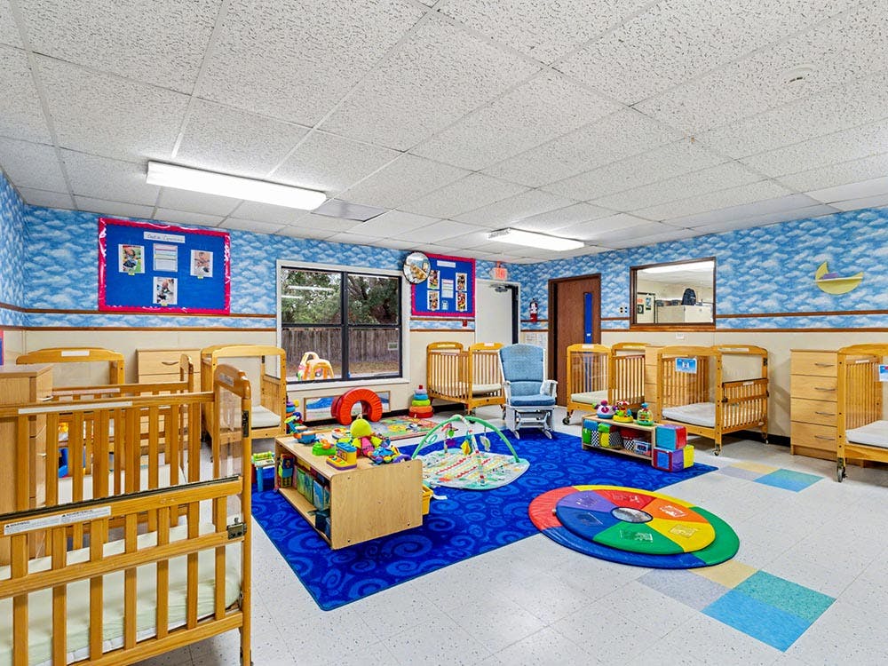 A brightly lit nursery room with multiple wooden cribs and infant play areas