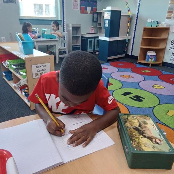 Child writing in a notebook at a desk in a classroom