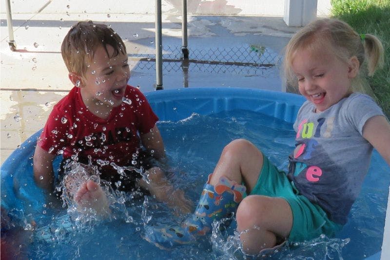 Two children splashing in a blue wading pool