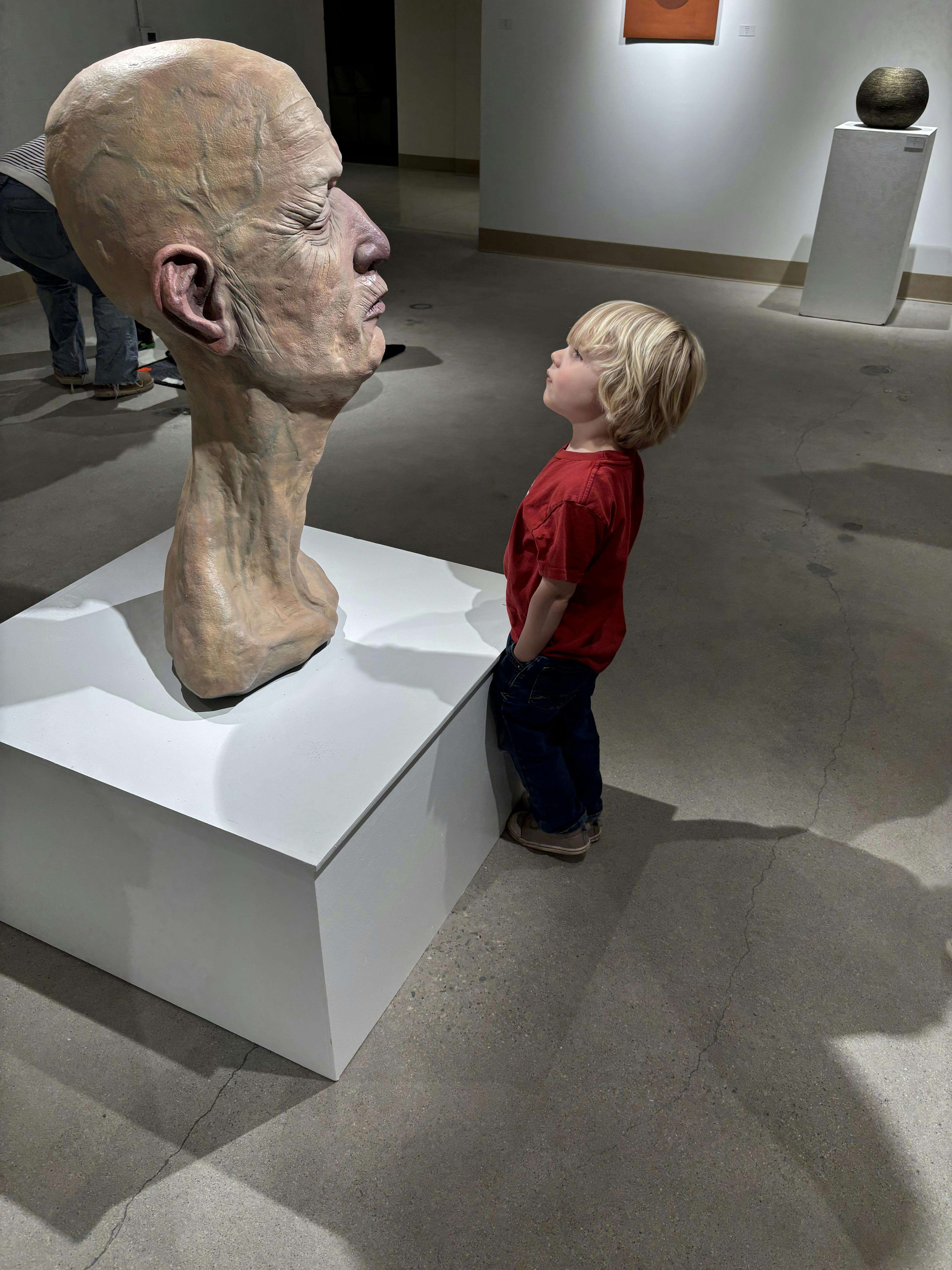 Child looking at a large human head sculpture in an art gallery