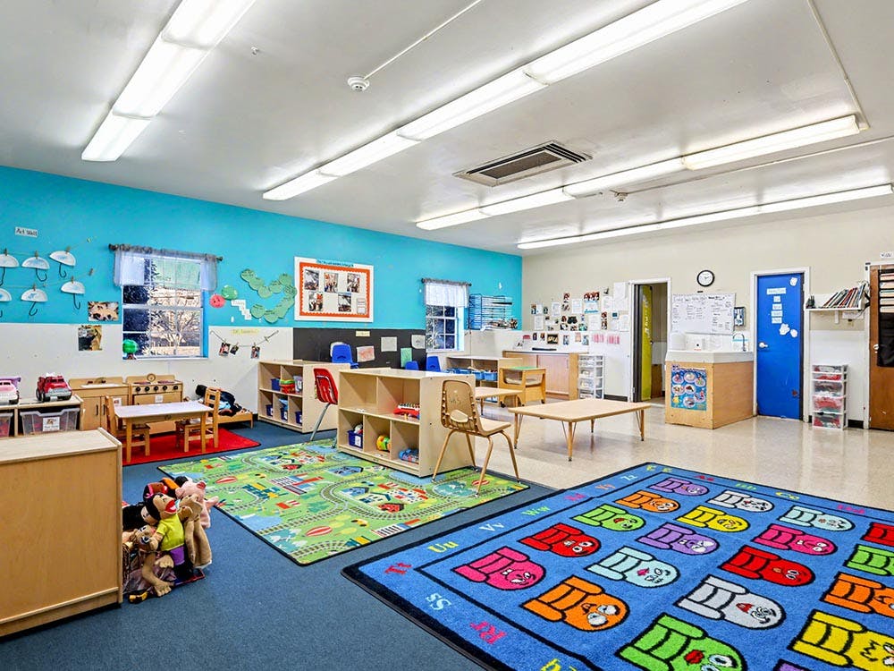 Classroom with blue walls, small tables and chairs, and play rugs