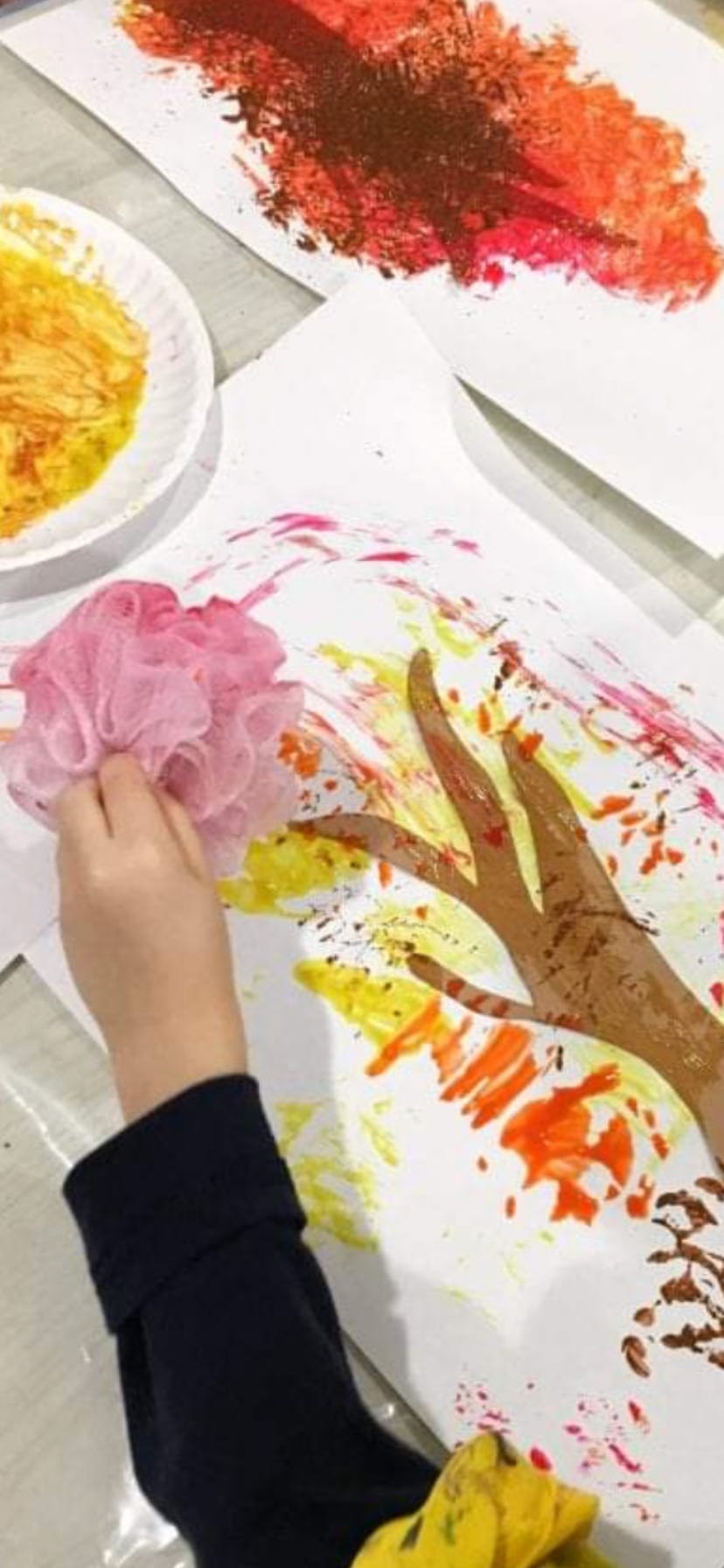 Child's hand holding a pink bath pouf to paint on paper