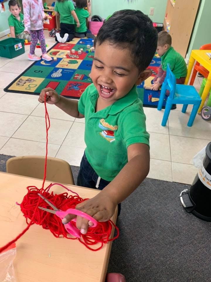 Child cutting red yarn with scissors in a classroom