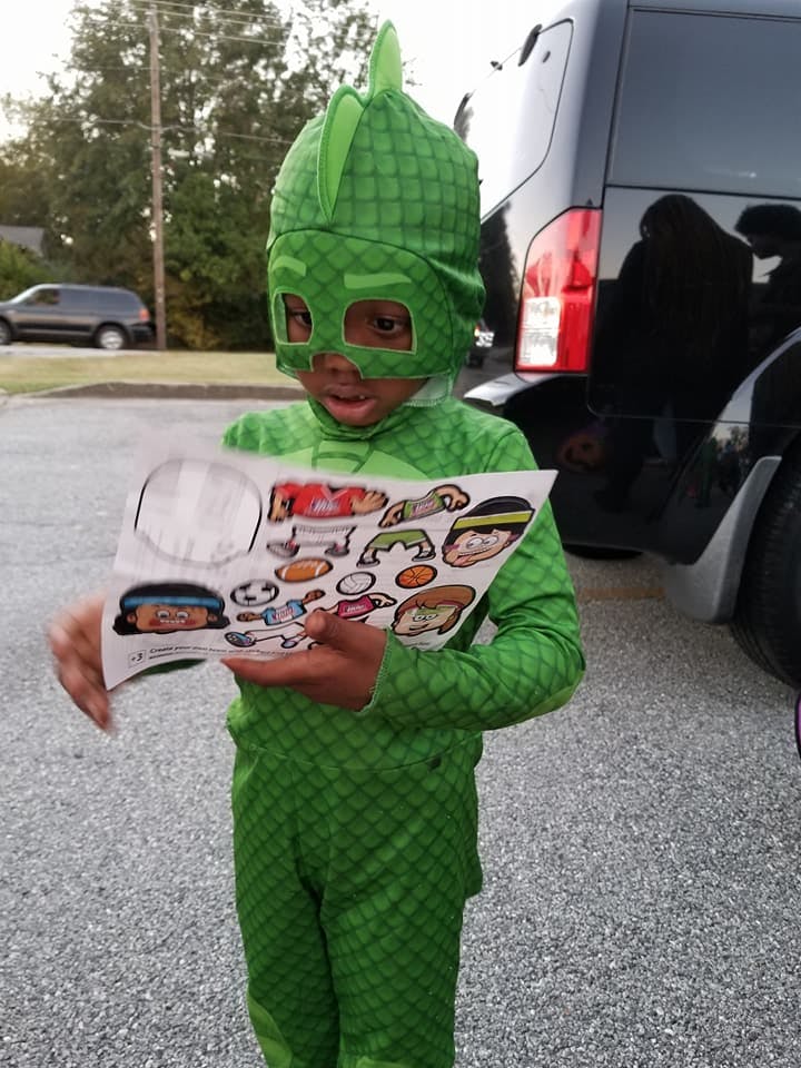 Child in green costume holding a sheet of stickers