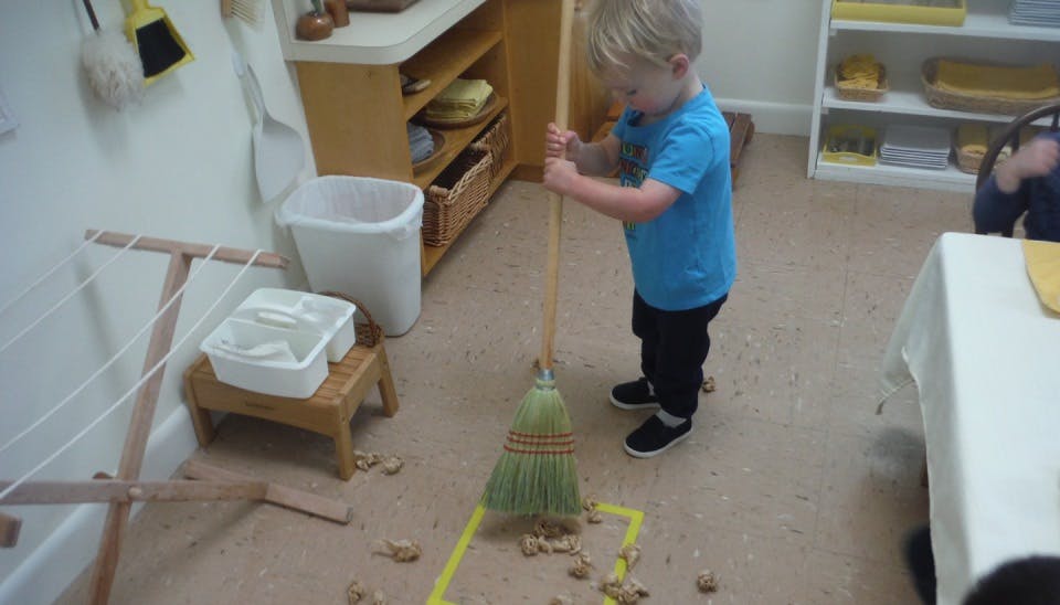 Child sweeping with a broom in a classroom