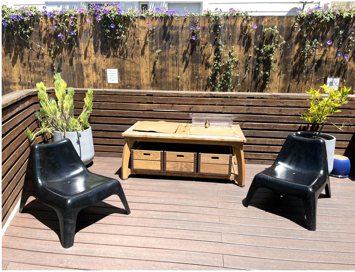 Outdoor patio with two black chairs, a wooden table, and potted plants