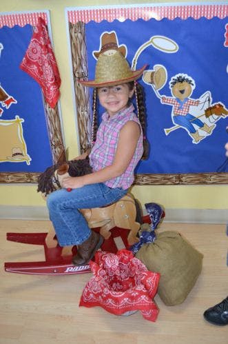 Child in a cowboy hat sitting on a rocking horse