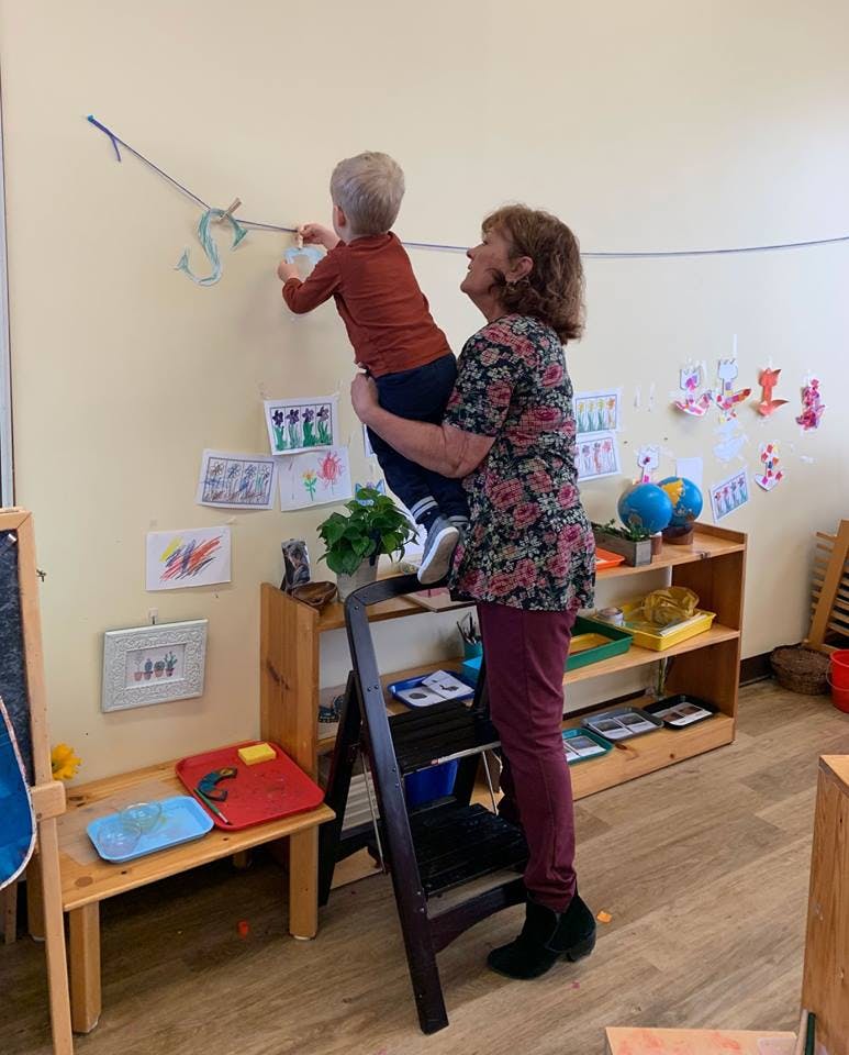 Person holding a child up to hang something on a string in a classroom