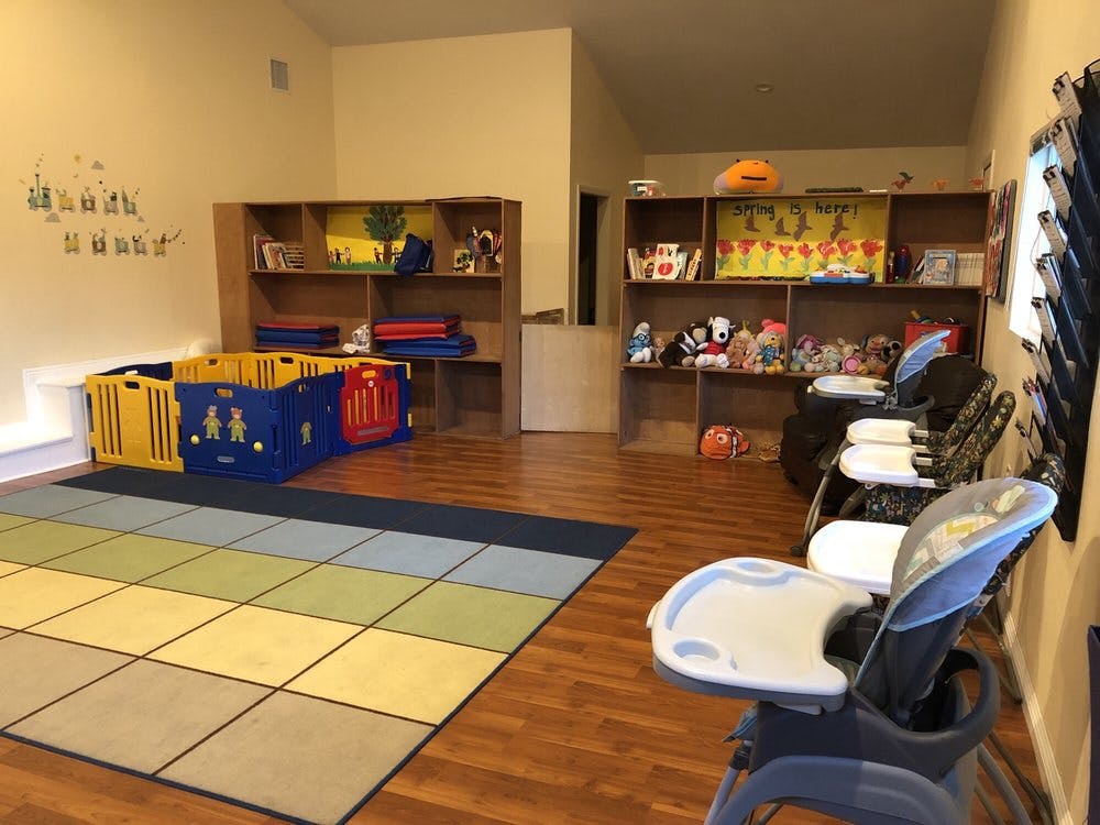Playroom with a colorful rug, playpen, shelves with toys, and high chairs