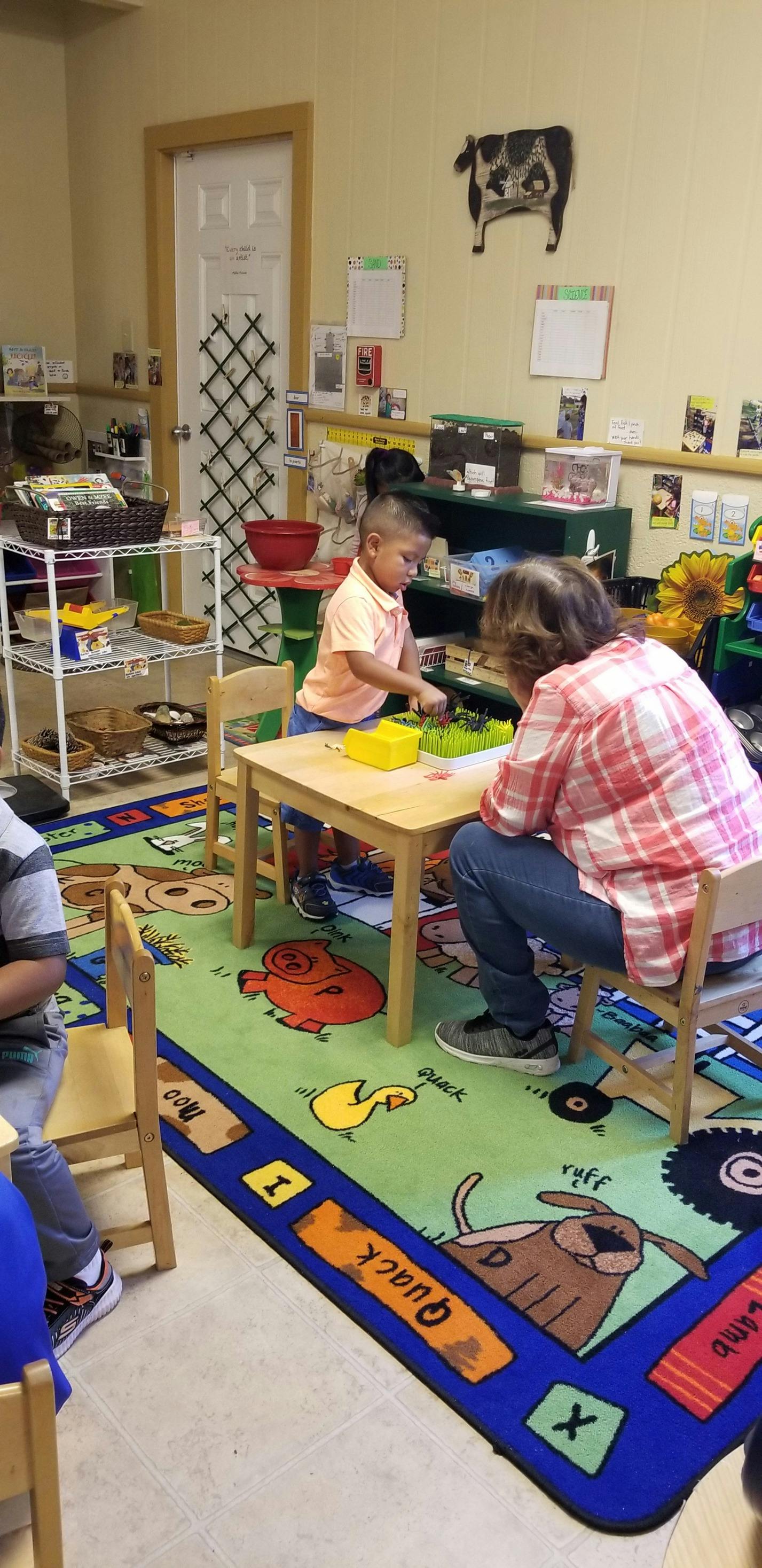 Child and adult playing with toys at a small table in a classroom
