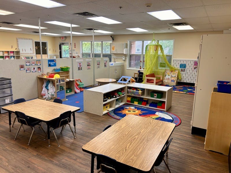 Empty classroom with small tables and chairs, play areas, and educational supplies