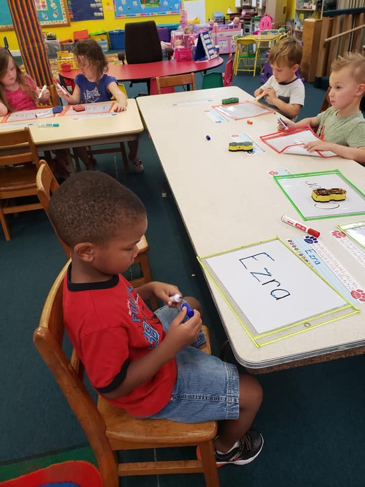 Children drawing and writing at tables in a classroom