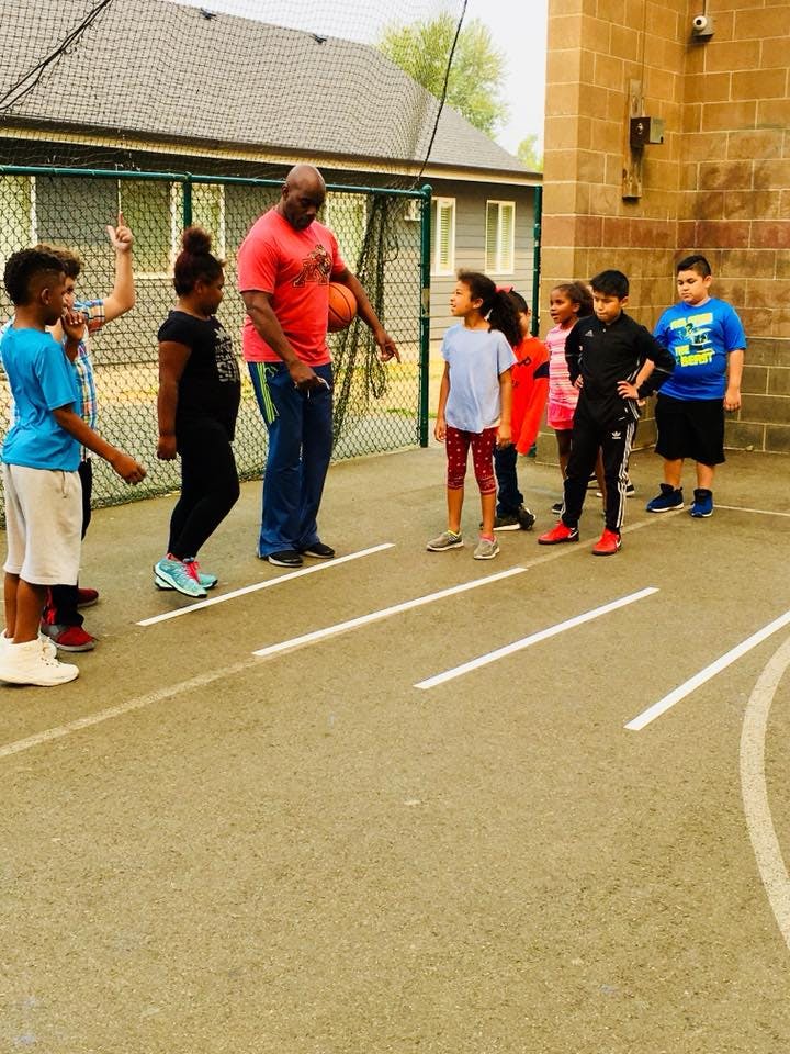 Adult with basketball instructing children on a court
