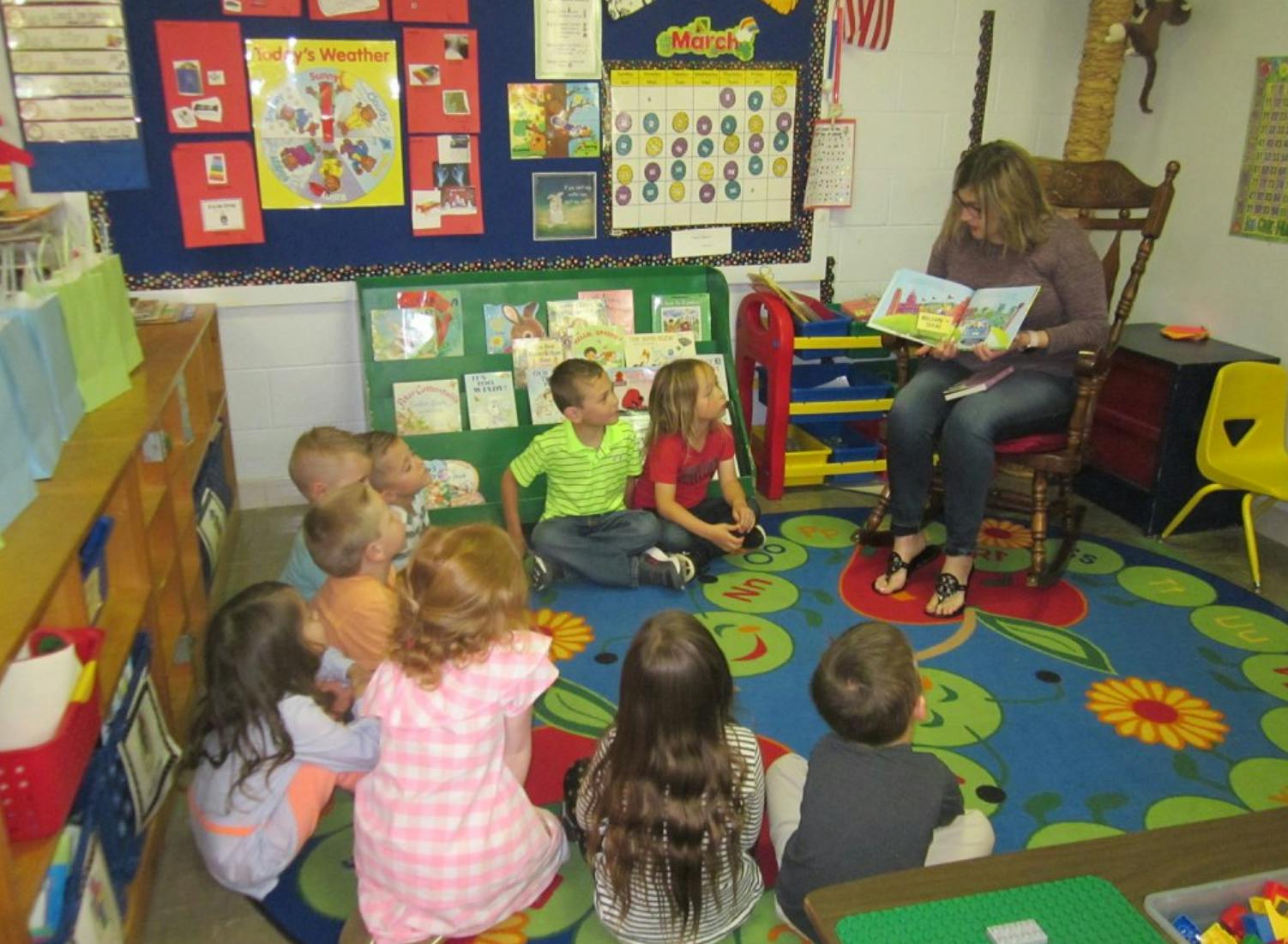 Adult reading a book to a group of children sitting on a rug
